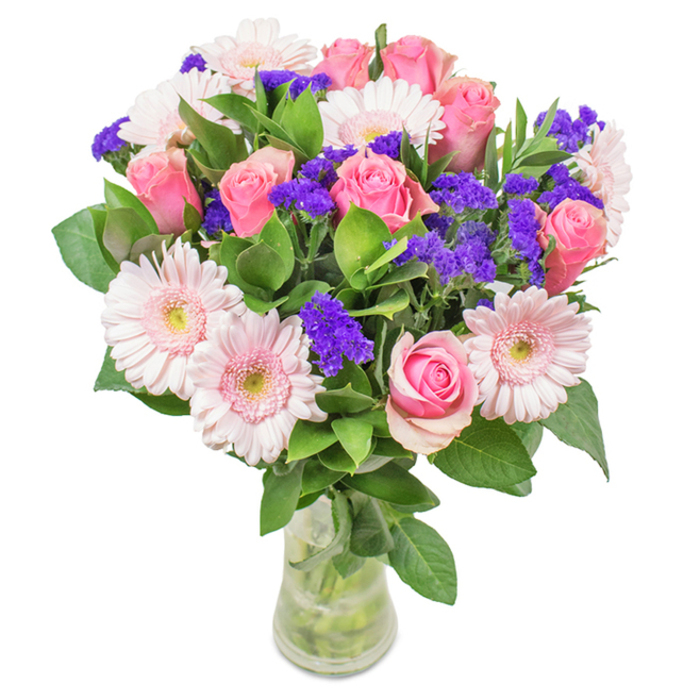 A captivating bouquet of pink roses, gerbera daisies, and purple statice displayed in a clear glass vase, thoughtfully arranged against a crisp white background. Central to the design are seven to nine soft-to-medium pink roses in varied stages of bloom-some tightly spiraled, others just unfurling-offering a sense of tenderness and celebration, much like family gatherings near Mortlake Green. Intertwined are around five to seven pale pink gerbera daisies, their broad petals and lighter centres recalling the openness of the riverside parks nearby. Vivacious purple statice fills the spaces in-between, adding depth and striking accent notes reminiscent of local summer festival bouquets. All rest above a romantic bed of deep green foliage, lush and abundant, grounding the composition and capturing the freshness of early morning in Mortlake. The glass vase showcases sturdy stems and glistening water, suggesting a just-delivered freshness, perfect for gift-giving or as a charming accent along Lower Richmond Road. This bouquet is ideally suited for celebrating birthdays, anniversaries, or simply as a gesture of thoughtfulness-a harmoniously blended arrangement from Flowers Mortlake, crafted to convey joy, admiration, and affection.